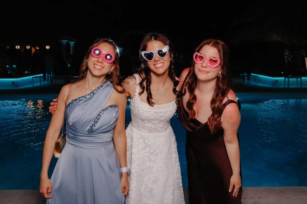 Sposa e amiche con occhiali a cuore a bordo piscina di sera